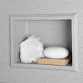 Recessed shelf in a gray shower wall holding soap and a sponge